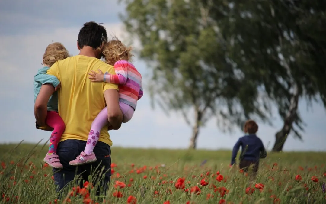 man carrying to girls on field of red petaled flower